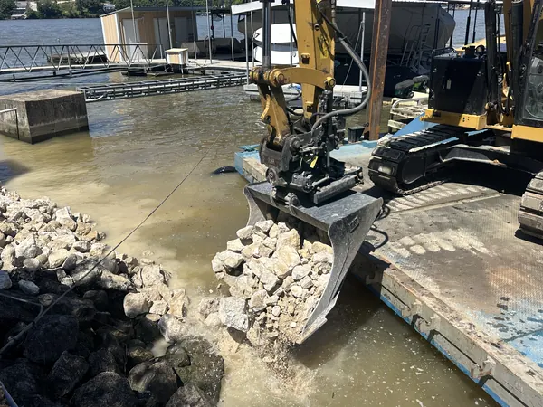 Excavator bucket placing rock from the barge